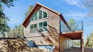A log cabin with a balcony, large windows, and a clear sky.