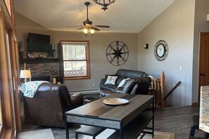 Una sala de estar con chimenea, sofá de cuero, mesa de comedor y ventilador de techo.