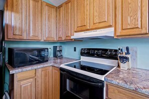 Una cocina con armarios de madera, microondas, estufa y cafetera.