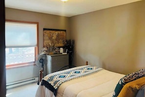 Un dormitorio con cama, cómoda, ventilador y ventana con persianas.