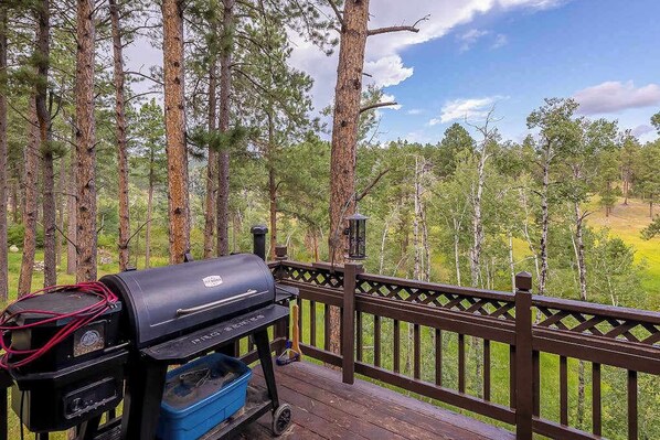 A barbecue grill on a wooden deck with a view of a forested area.