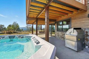 A hot tub with a wooden pergola overhead, a barbecue grill, and a stone wall.