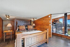 Quarto com cabeceira de madeira, cama com roupa de cama estampada, duas luminárias de cabeceira e vista para a varanda.