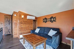 Quarto com parede de madeira, sofá azul, mesa de centro de madeira e um objeto decorativo na parede.