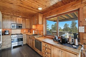 A kitchen with wooden cabinets, stainless steel appliances, and a large window offering a view of trees.