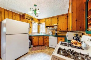 Eine Küche mit Holzschränken, einem Kühlschrank, einem Herd und einer Kaffeemaschine.