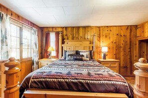Ein Zimmer mit Holzwänden, einem Bett, zwei Nachttischen und einem Fenster mit Vorhängen.