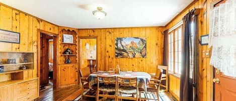 A wooden interior with a dining table, chairs, and a painting on the wall.