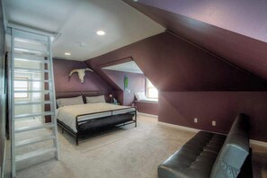 Ein Schlafzimmer mit schrägem Dach, einem Bett, einer Bank und einer Leiter.