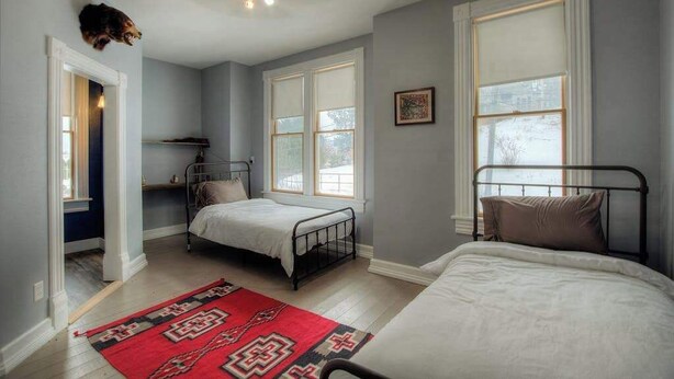 A bedroom with two beds, a red patterned rug, and large windows.