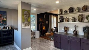 A modern kitchen with a central island, dark cabinetry, and a variety of decorative items on shelves.