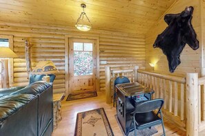 Ein rustikales Holzhaus-Interieur mit einer Couch, einem Tisch, einem Stuhl, einem aufgehängten Tierfell und einem Buntglasfenster.