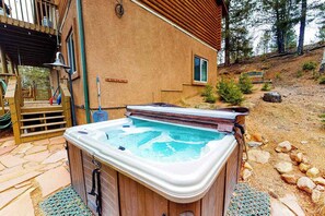 A hot tub in a backyard with a wooden deck and a house in the background.