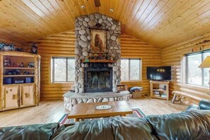 Ein Blockhaus-Interieur mit Kamin aus Stein, Holzwänden, einem Fernseher und einer Ledersofa.