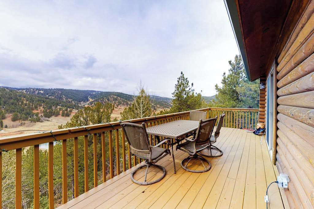 A wooden deck with a table and chairs, overlooking a forested landscape.