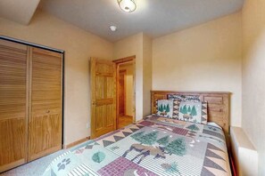 A bedroom with a bed, wooden wardrobe, and a door leading to another room.