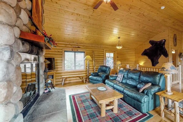 Ein rustikales Blockhaus-Interieur mit Kamin aus Naturstein, Ledersofa und einem aufgehängten Tierkopf.