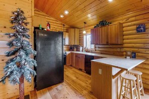 Eine Küchenzeile im Blockhausstil mit Holzwänden, einem schwarzen Kühlschrank, Holzschränken und einer kleinen Kochinsel mit Hockern.