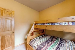 Ein Stockbett mit gemustertem Bettbezug, eine Holztür und eine schräge Decke.