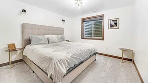 Un dormitorio con una cama grande, una ventana con persianas, una mesita de noche y una lámpara de pared.