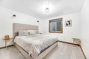 Ein Schlafzimmer mit einem großen Bett, einem Fenster mit Jalousien, einem Nachttisch und einer Wandleuchte.