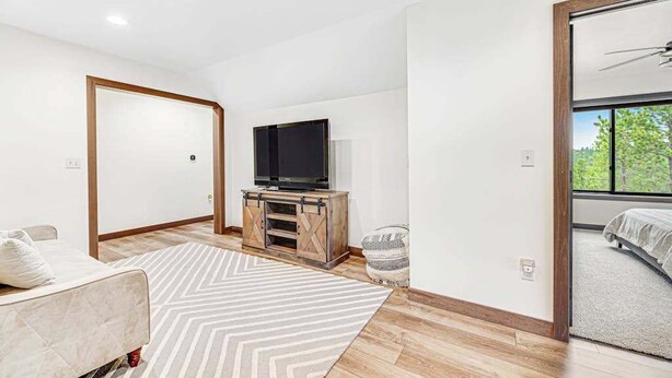 Una sala moderna con sofá, televisor sobre un mueble de madera, alfombra estampada y un ventanal con vistas a zonas verdes.