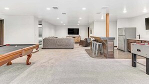 Una sala de estar moderna con mesa de billar, un sofá y una zona de cocina con barra.
