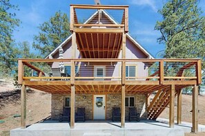 Eine mehrstöckige Holzkonstruktion mit einer zentralen Treppe, einer Tür mit einem Kranz und zwei Bänken vor der Fassade.