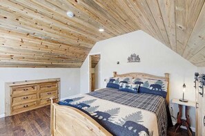 Ein Schlafzimmer mit Holzboden, einem Bett mit Bettwäsche zum Thema Wald, einer Holzkommode und einem kleinen Nachttisch mit Lampe.