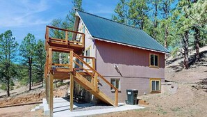 A single-story house with a wooden staircase leading to a balcony, surrounded by trees. - Five Mile Retreat- Spacious Retreat • Large Deck & WiFi (Cripple Creek)