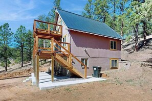 Ein einstöckiges Haus mit einer Holztreppe, die zu einem Balkon führt, umgeben von Bäumen.