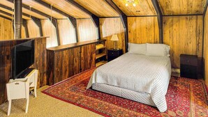 Quarto com uma cama, televisão, abajur e teto de madeira.