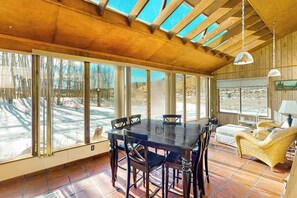 A dining area with a large table and chairs, a sofa, and large windows with a view of a snowy landscape. - Rainbows End - Mountain-View Home • Basketball Court (Cripple Creek)