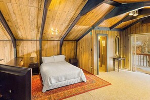 A bedroom with a bed, a nightstand, a lamp, a wooden ceiling, and a door leading to another room. - Rainbows End - Mountain-View Home • Basketball Court (Cripple Creek)