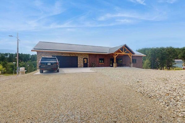 A two-story building with a garage, a driveway, and a gravel lot. - Bear Butte Retreat - Private Hot Tub Retreat • Secluded (Deadwood)