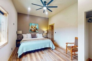 Une chambre à coucher avec un lit, un ventilateur de plafond, un tableau, une chaise et un plancher en bois.