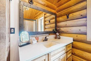 Ein Holzhütten-Innenraum mit einem großen Spiegel, einem weißen Waschbecken und Holzschränken.