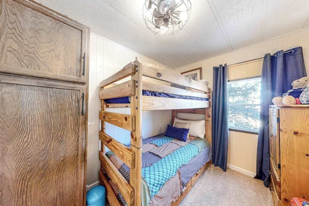 A bunk bed with a wooden headboard, a window with curtains, and a ceiling fan.