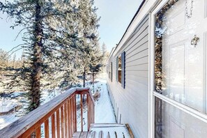 Eine Holzdielenfläche führt zu einem Haus mit einer weißen Tür, umgeben von schneebedeckten Bäumen.