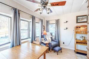 Ein Zimmer mit einem Holztisch, einem blauen Sessel, einem Deckenventilator und einem Bücherregal.