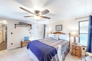 A bedroom with a bed, a ceiling fan, a bedside table with a lamp, a dresser, and a window with curtains. - Dog-Friendly Rustic Cabin w/ Fireplace (Florissant)
