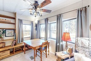 Ein gemütliches Zimmer mit einem Holzesstisch, einem Deckenventilator und einem Fenster mit Vorhängen.