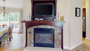 Ein Wohnzimmer mit Kamin, einem darüber montierten Fernseher und einem Essbereich mit Tisch und Stühlen.