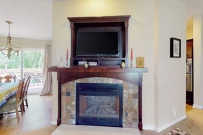 Ein Wohnzimmer mit Kamin, einem darüber montierten Fernseher und einem Essbereich mit Tisch und Stühlen.