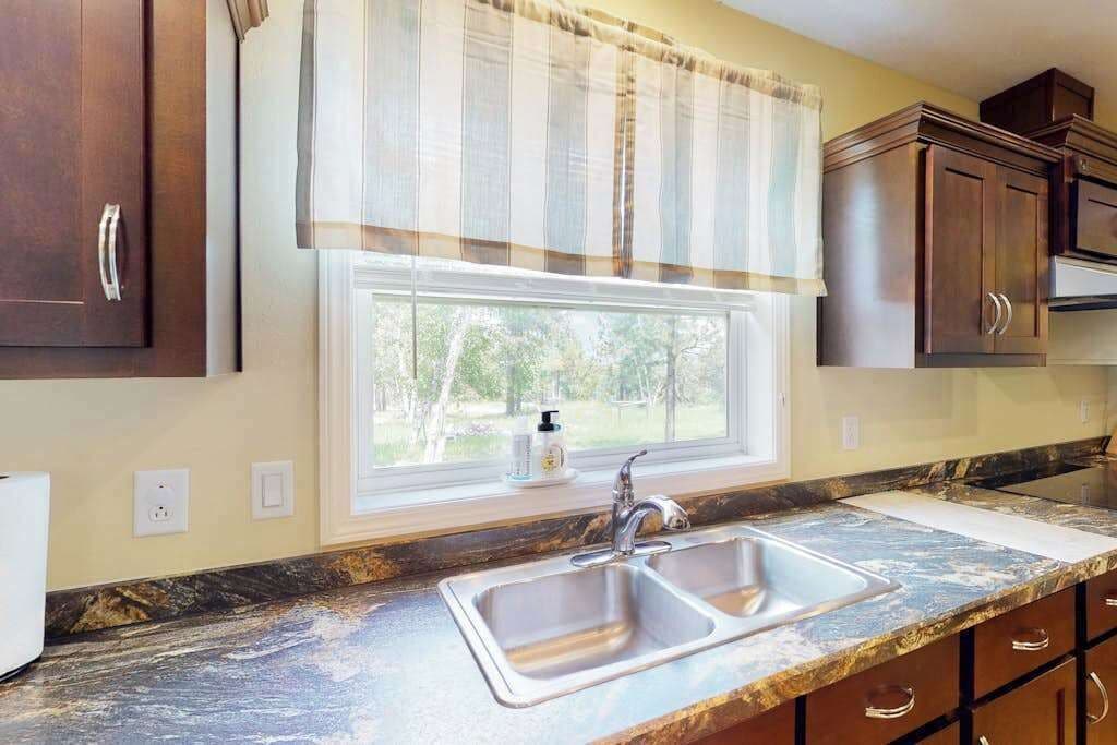 A kitchen with a double sink, wooden cabinets, a window with a view, and a marble countertop.