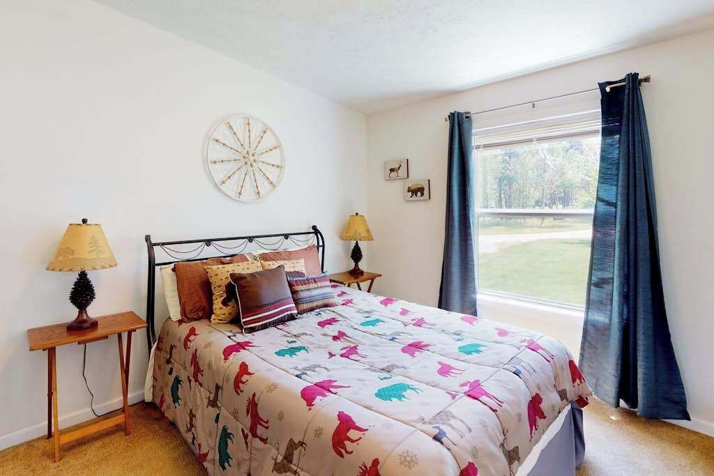 Un dormitorio con una cama, dos mesitas de noche, una ventana con cortinas y un reloj de pared.