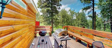 Eine Holzterrasse mit Grill, Bank und Tisch.