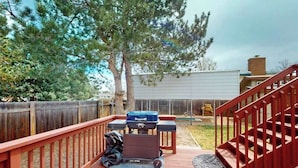 A wooden deck with a barbecue grill, a red staircase, and a fenced backyard. - Springs Sanctuary - Dog-Friendly Home • Decks & Fireplaces (Colorado Springs)