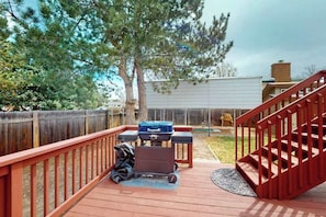 A wooden deck with a barbecue grill, a red staircase, and a fenced backyard. - Springs Sanctuary - Dog-Friendly Home • Decks & Fireplaces (Colorado Springs)