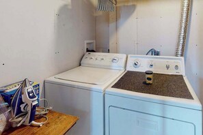 A laundry room with two washing machines and a dryer, a wooden table with a coffee maker, and a vent on the wall. - Springs Sanctuary - Dog-Friendly Home • Decks & Fireplaces (Colorado Springs)